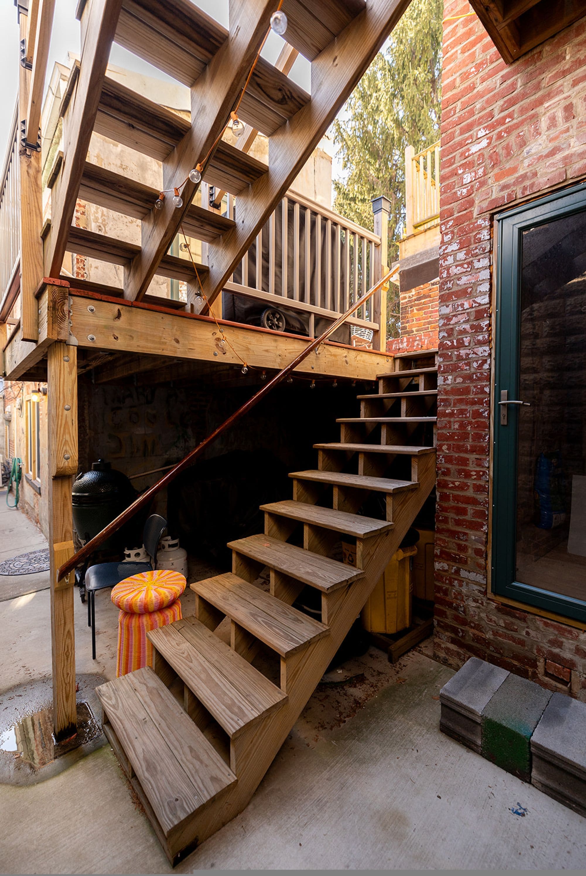 Una escalera de madera que lleva a una zona superior con una pared de ladrillo y una puerta.