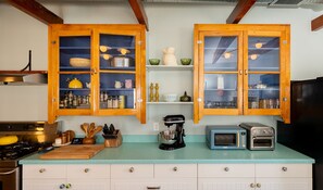 A kitchen with wooden cabinets, a countertop, a stove, a coffee maker, a toaster, and a microwave. - Wyatt's Saloon Guest House 2 (Baltimore)