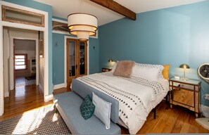 A bedroom with a bed, bedside tables, a bench, a mirror, and a door leading to another room. - Wyatt's Saloon Guest House 2 (Baltimore)