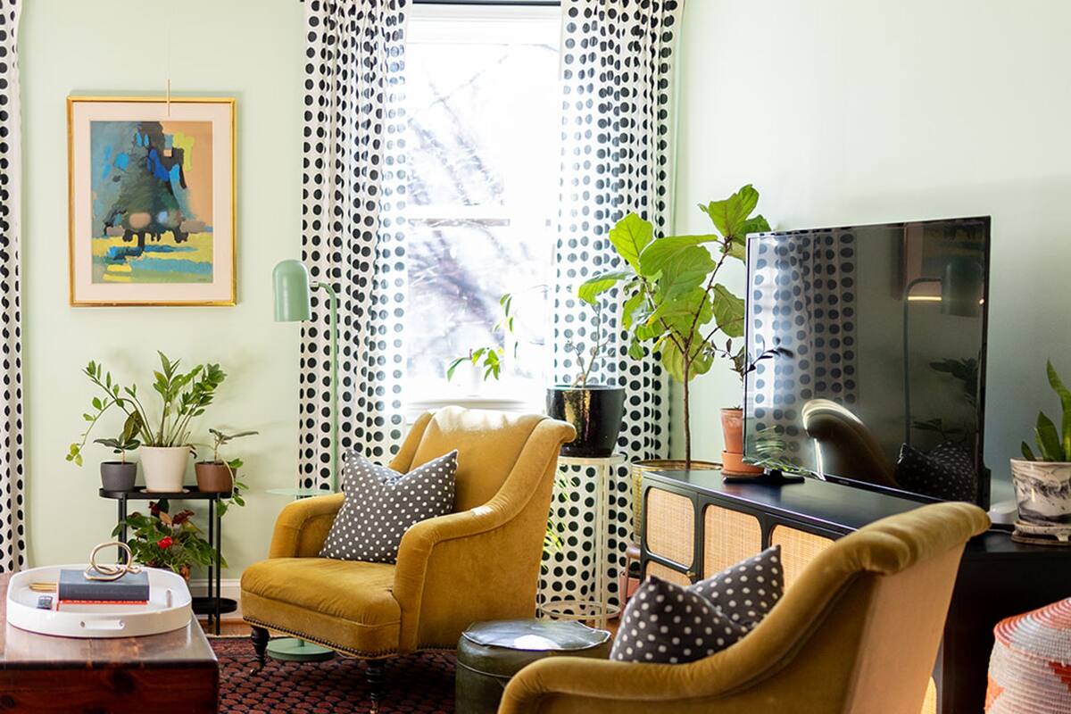 A living room with a yellow armchair, a black TV stand, and a patterned rug.