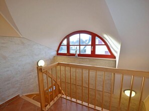 Experience the airy feel of this loft-style room with a high ceiling and a wooden staircase leading to a cozy landing with a window offering a view of the outside.