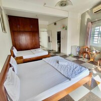 Una habitación de hotel con dos camas, un armario de madera, una mesita y un ventilador.
