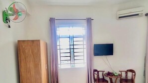 A room with a large window, a TV mounted on the wall, a wooden cabinet, and a small table with chairs. - Hoang Nam Hotel Q2 SG- by Bay Luxury (Ho Chi Minh City)