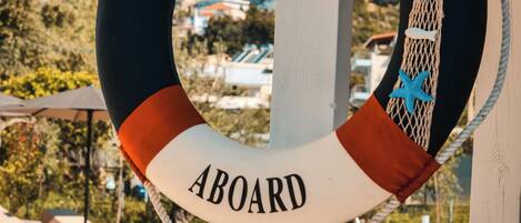 En redningskranz med teksten "WELCOME ABOARD", en pool, udendørs siddepladser og et bjerglandskab i baggrunden.