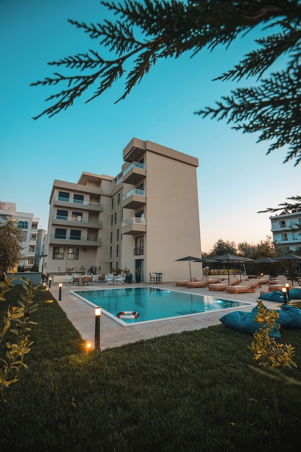 A pool area with lounge chairs and umbrellas, surrounded by a building with multiple balconies.