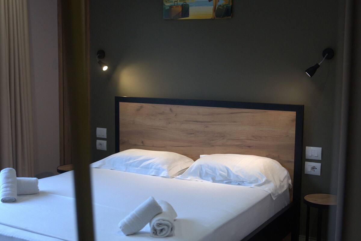 A neatly made bed with white linens and towels, a painting on the wall, and a small table beside the bed.
