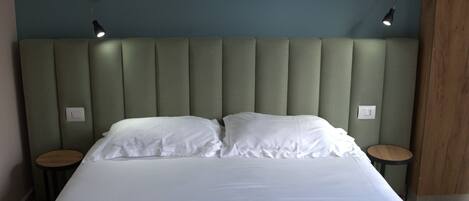 A neatly made bed with white linens and towels, a padded headboard, and two bedside tables with lamps.