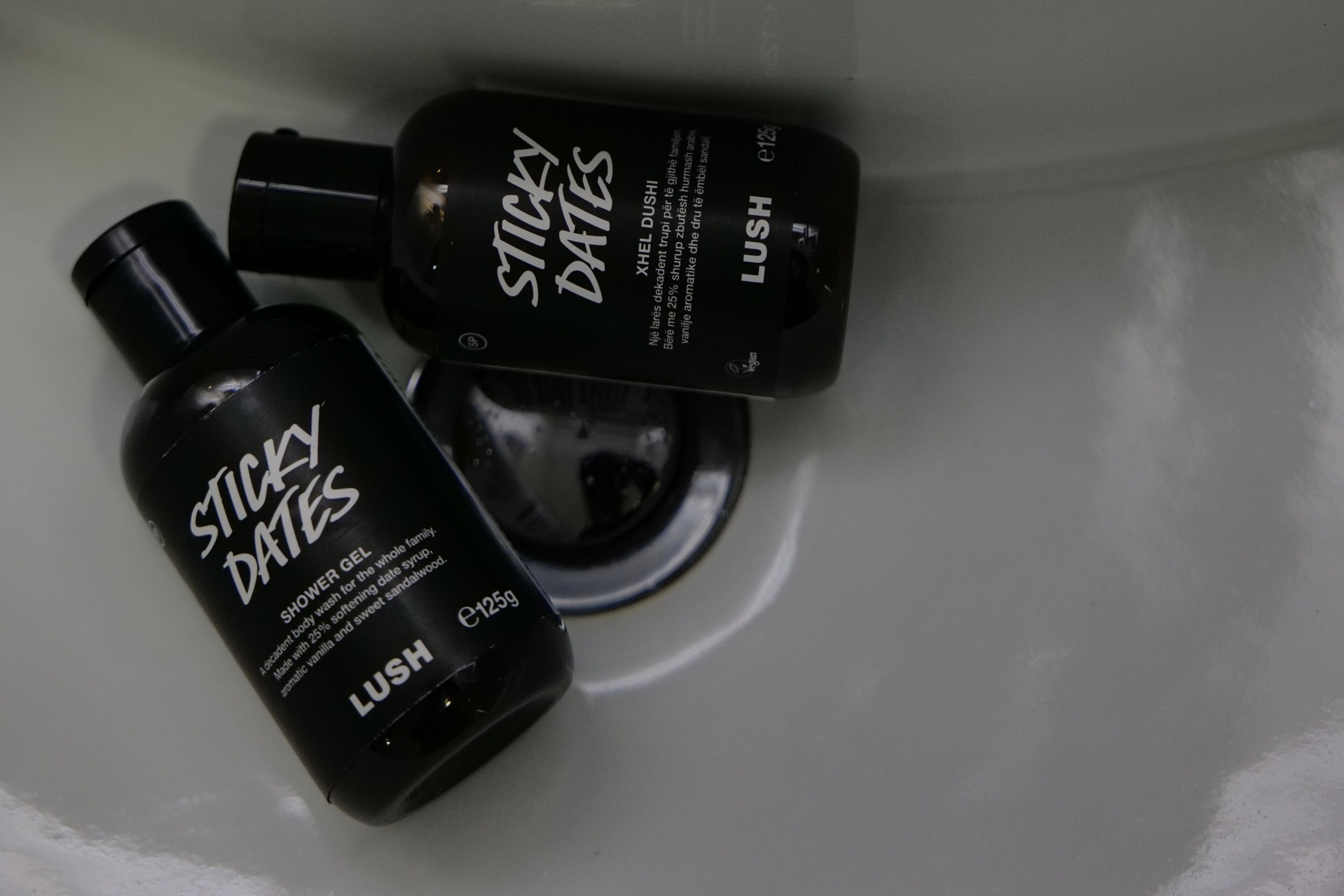 Two bottles of 'Sticky Dates' shower gel in a sink.