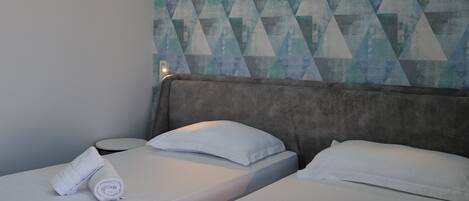 A hotel room with two beds, each with a neatly folded towel. The room features a geometric patterned wall and a modern headboard.