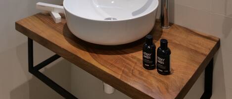 A modern bathroom with a round white sink, a rectangular mirror with LED lighting, and two small bottles on a wooden countertop.