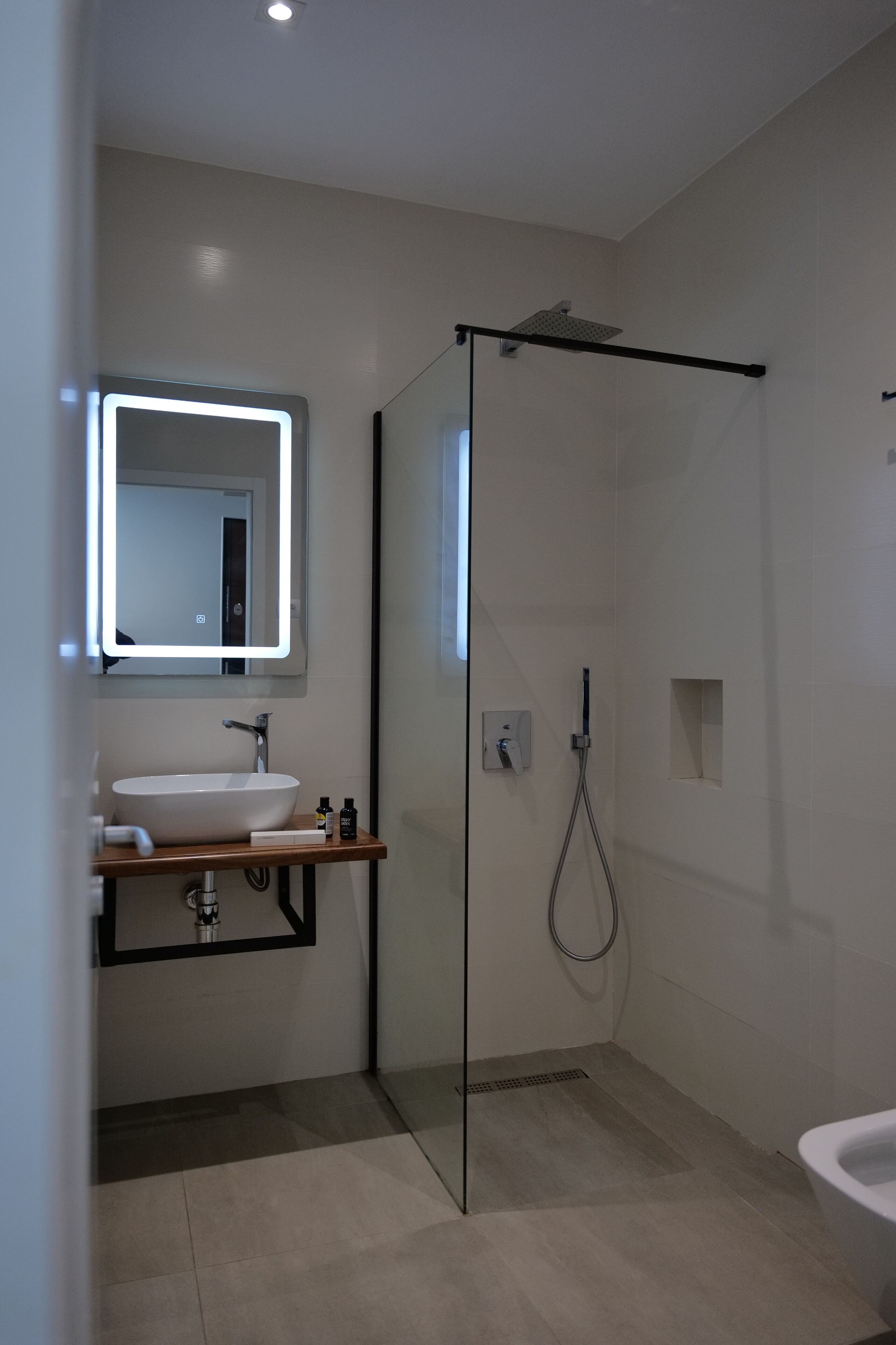 Un baño moderno con ducha envuelta en vidrio, un lavabo blanco y un espejo con iluminación integrada.