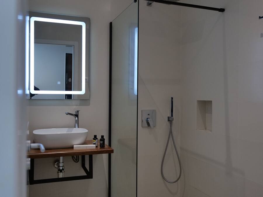 Un baño moderno con ducha envuelta en vidrio, un lavabo blanco y un espejo con iluminación integrada.