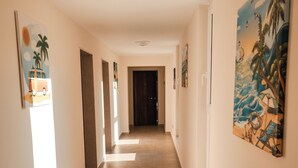 A long, well-lit hallway with tiled floors and walls adorned with tropical-themed artwork. - The Blue Wave Hotel (Himarë)