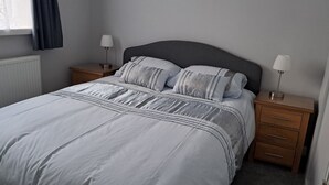 A neatly made bed with a grey headboard, two bedside tables with lamps, and a window with curtains. - 2 bedroom chalet bungalow, short drive to The New Forest and Bournemouth beaches (Poole)
