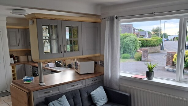 A modern kitchen with grey cabinets, a wooden countertop, and a grey sofa near a window with a view of a street and greenery. - 2 bedroom chalet bungalow, short drive to The New Forest and Bournemouth beaches (Poole)