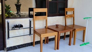 A wooden table and two chairs in a room with a tiled floor, a window, and a shelf with shoes. - Pondok Dete Guesthouse (Denpasar)