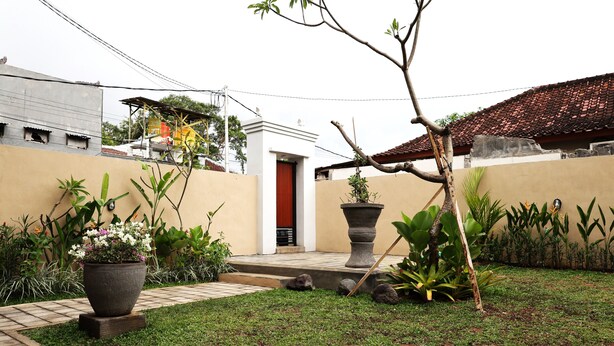 A courtyard with a paved walkway, potted plants, and a red door. - Pondok Dete Guesthouse (Denpasar)