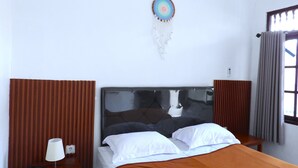 A hotel room with a bed, a bedside lamp, a dreamcatcher, and a window with curtains. - Pondok Dete Guesthouse (Denpasar)