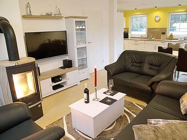 A living room with a TV, fireplace, sofa, and a small dining area with a kitchen in the background.
