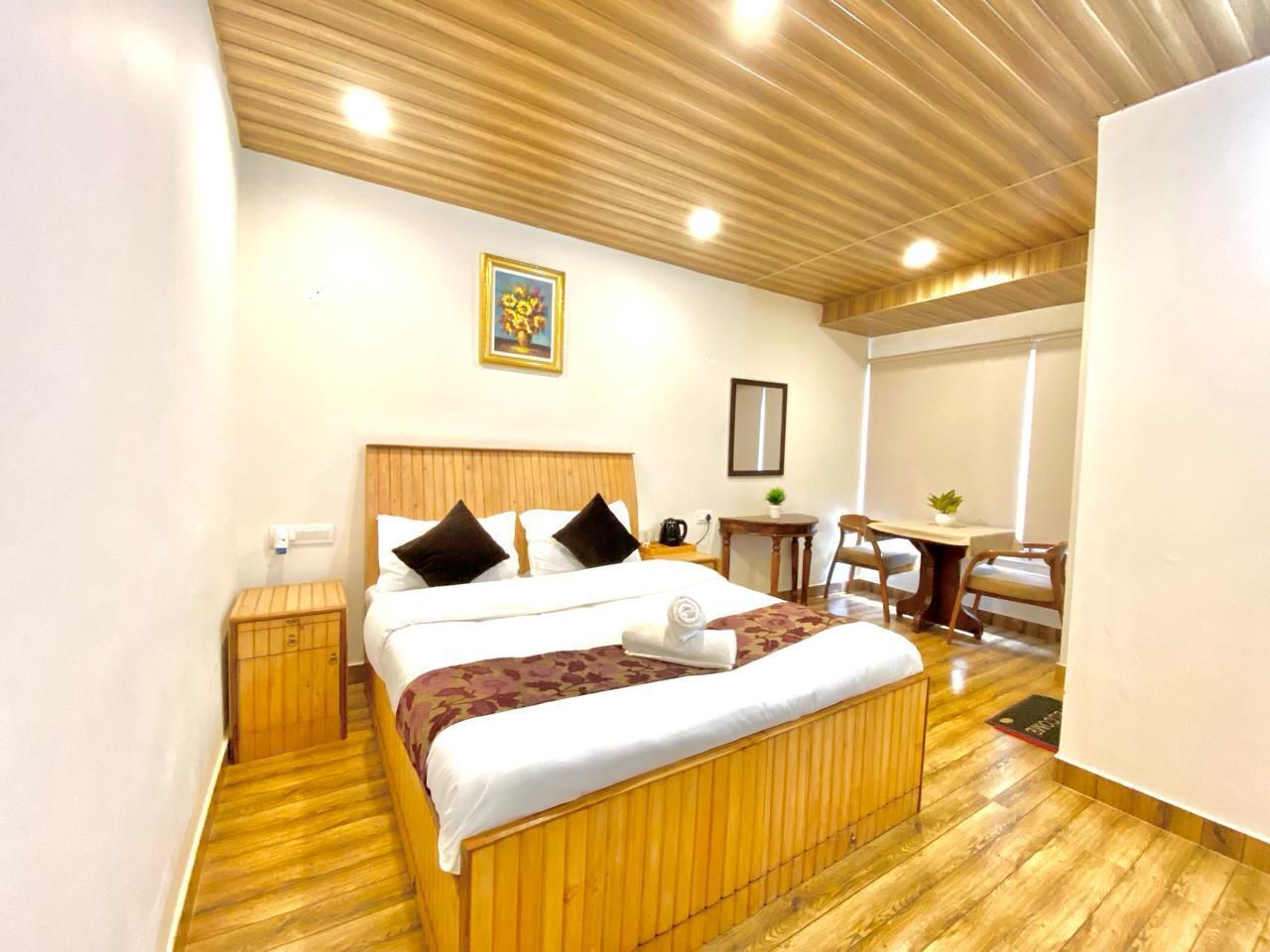 A hotel room with a wooden bed, a small bedside table, a chair, a desk, and a window.