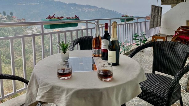 A balcony with a table set for two, featuring a bottle of wine, two glasses, and a menu. - Kasauli View (Solan)