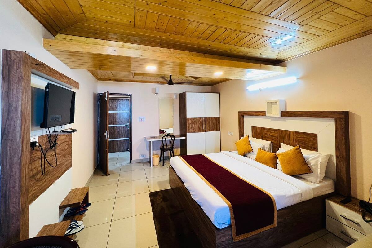 Ein Schlafzimmer mit Holzboden, einem Bett mit roter Decke, einem an der Wand montierten Fernseher und einem Schreibtisch mit Stuhl.