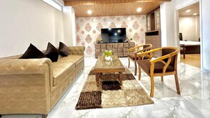 A modern living room with a sofa, coffee table, and chairs, a flat-screen TV, and a patterned wall. - Kasauli View (Solan)