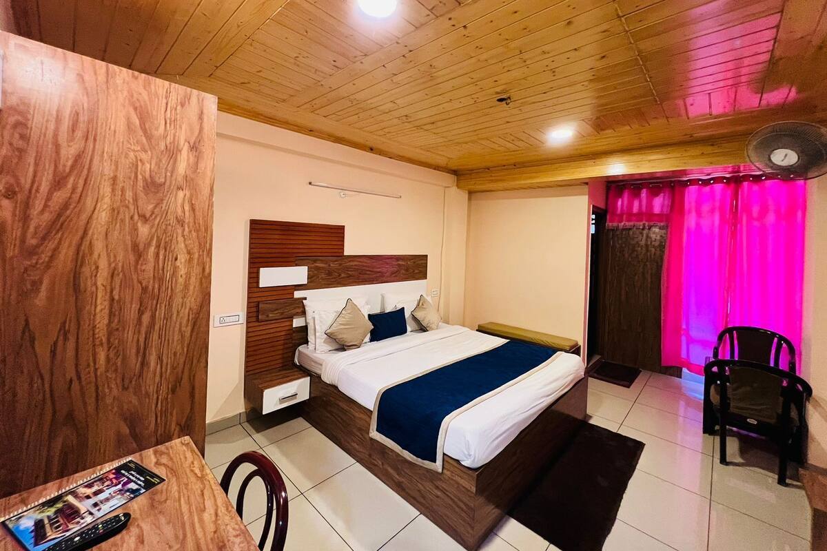 Ein Schlafzimmer mit Holzboden, einem Bett mit blauer Bettdecke, einem Nachttisch, einem Stuhl und einem Tisch mit Fernbedienung.