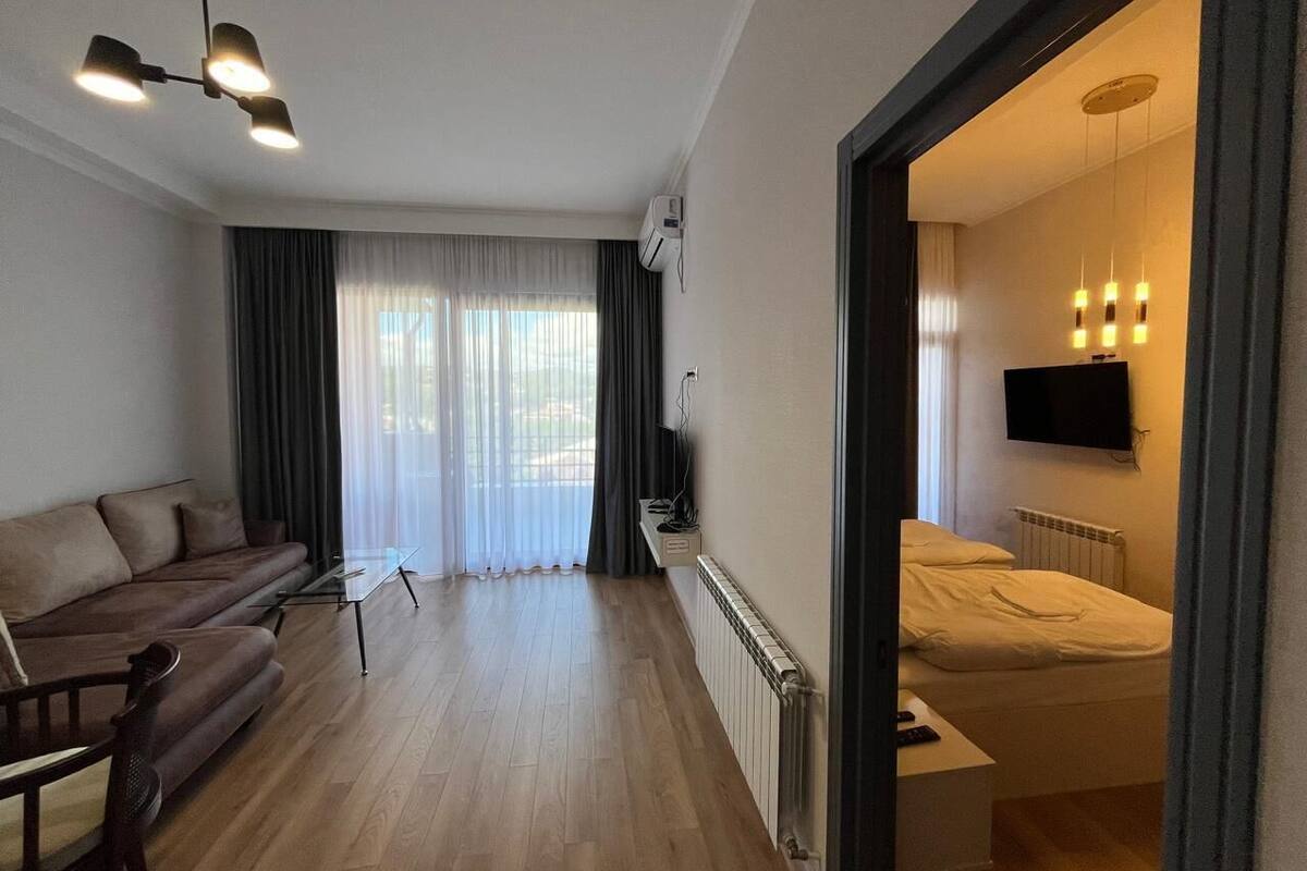 A modern hotel room with a sofa, a small table, a bed, and a TV.