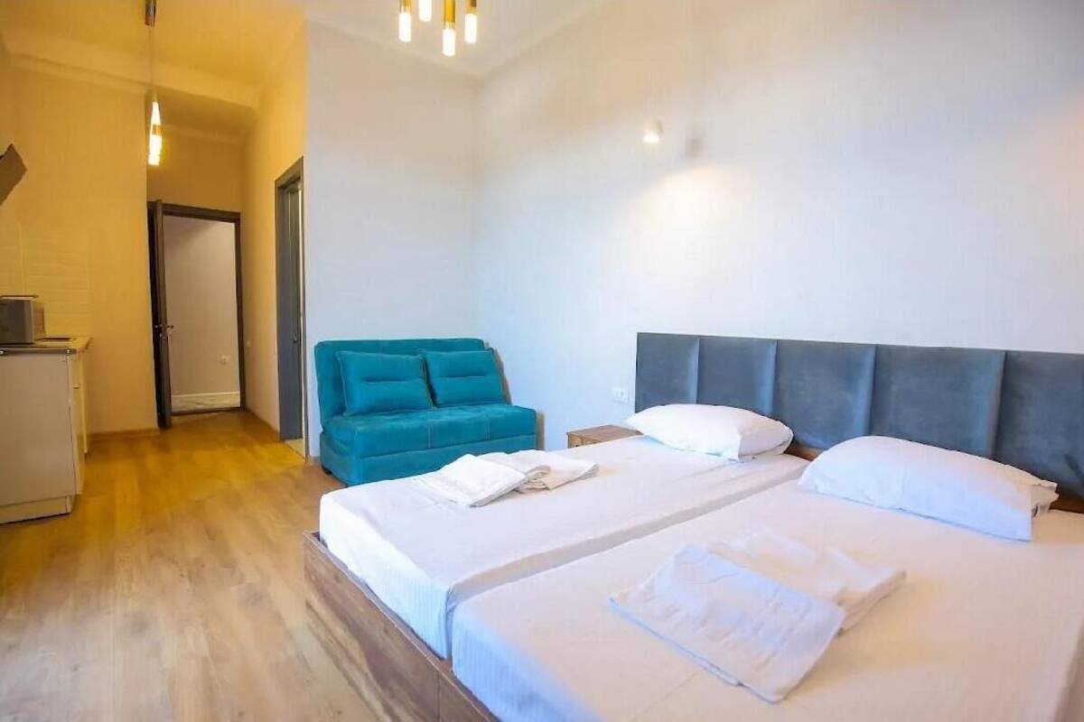 A hotel room with two beds, a blue armchair, and a small desk.