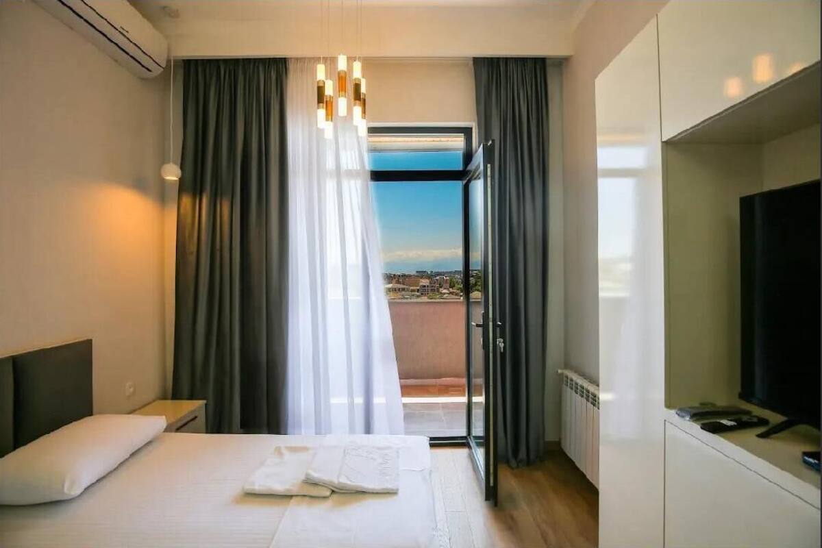 A hotel room with a bed, a desk, a TV, and a balcony with curtains.