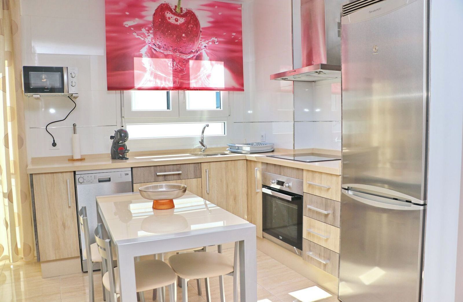 Een moderne keuken met een roestvrijstalen koelkast, een vaatwasser, een oven en een magnetron. Er staat een witte eettafel met twee stoelen en een decoratieve schaal erop.