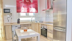 A modern kitchen with a stainless steel refrigerator, a dishwasher, an oven, and a microwave. There is a white dining table with two chairs and a decorative bowl on it. - Apartamento El Mirador (Conil de la Fra.)