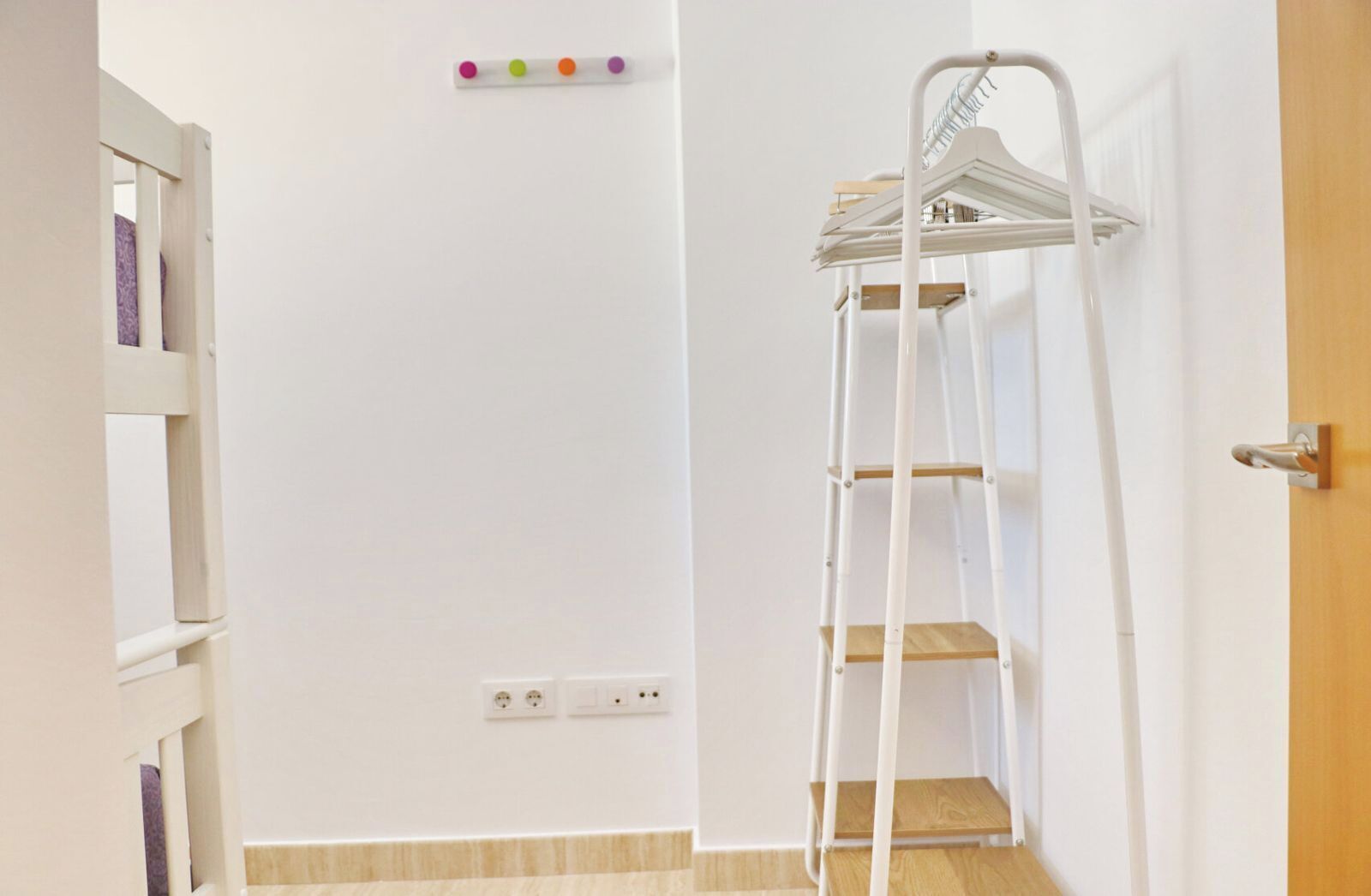 A room with a white wall, a wooden door, a white shelf unit, and a white ladder with shelves.