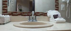 Un baño con lavamanos, espejo y una pila de toallas.