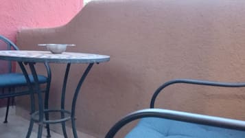 Un pequeño espacio al aire libre con una mesa redonda de metal y dos sillas, una con cojín azul.