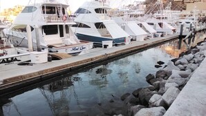 A marina with boats docked, a rocky shoreline, and a clear waterway. - María Elena (Cabo San Lucas)