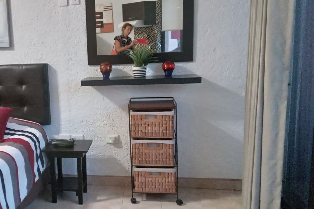 A bedroom with a bed, pillows, a nightstand, a mirror, and a shelf with decorative items.