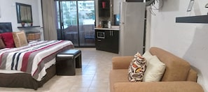 A bedroom with a bed, a sofa, a bench, a kitchenette, and a balcony with a view. - María Elena (Cabo San Lucas)