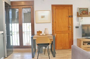A room with a wooden door, a framed picture on the wall, a table with chairs, and a television on a wooden stand.