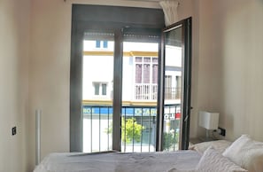 A bedroom with a bed, a nightstand, a lamp, and a view of a building through a sliding door.