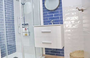 Een badkamer met een douchecabine van glas, een wit wastafelmeubel met twee lades, en een wand betegeld met blauwe tegels.