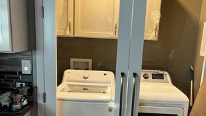 A laundry room with two white appliances, a dryer and a washer, and a countertop with a kettle and other items. - “Lovely” Bungalow near downtown Quincy!  (Quincy)