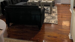 A living room with a sectional sofa, a coffee table, and a chandelier. There is a window with blinds, a door, and a rug on the wooden floor. - “Lovely” Bungalow near downtown Quincy!  (Quincy)