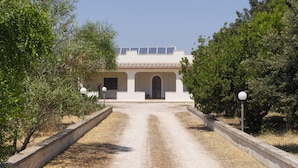 Un edificio de fachada blanca, paneles solares en el techo y un camino de grava que lleva a la entrada.