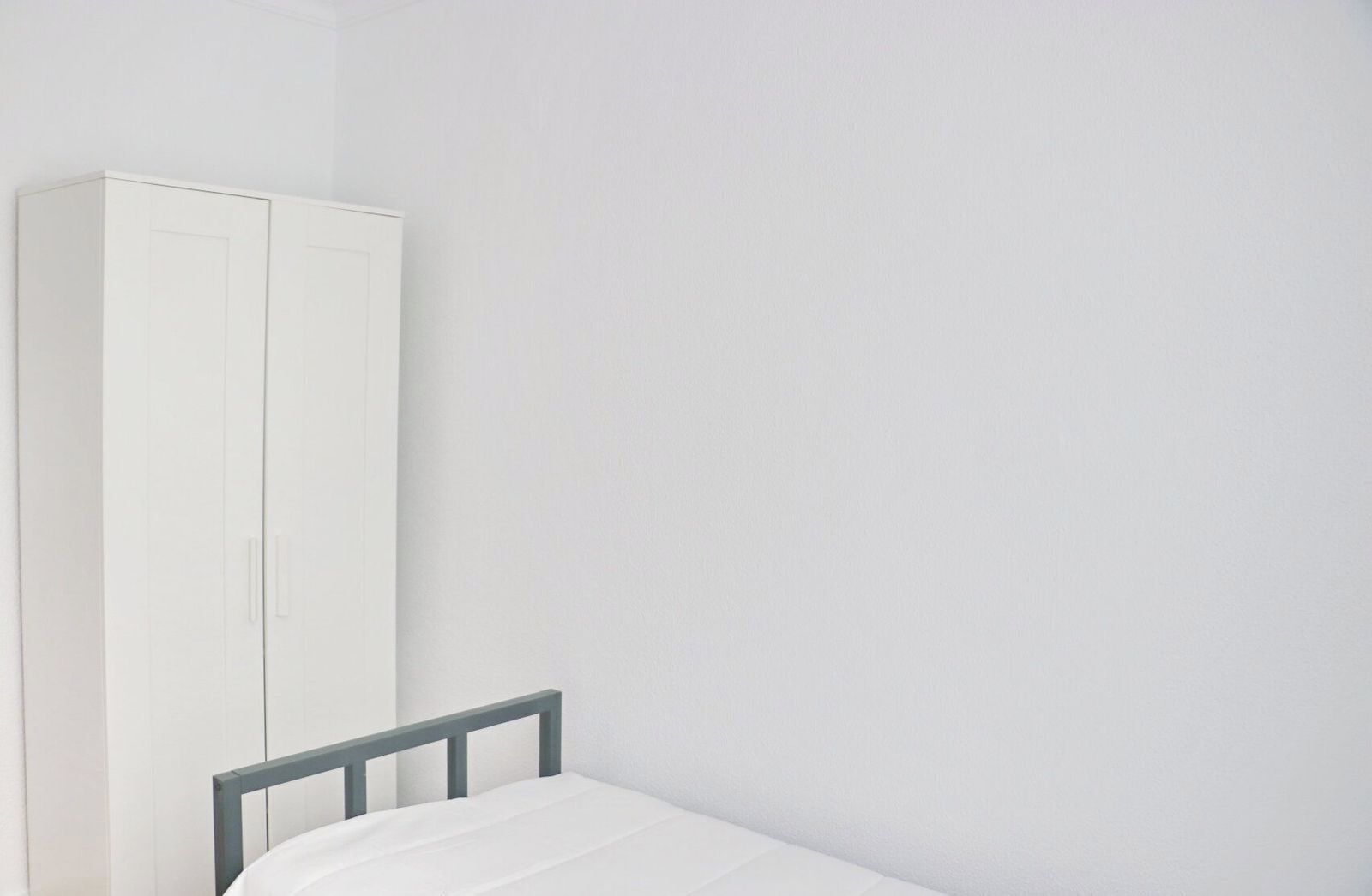 Quarto com uma cama de solteiro e um guarda-roupa branco.