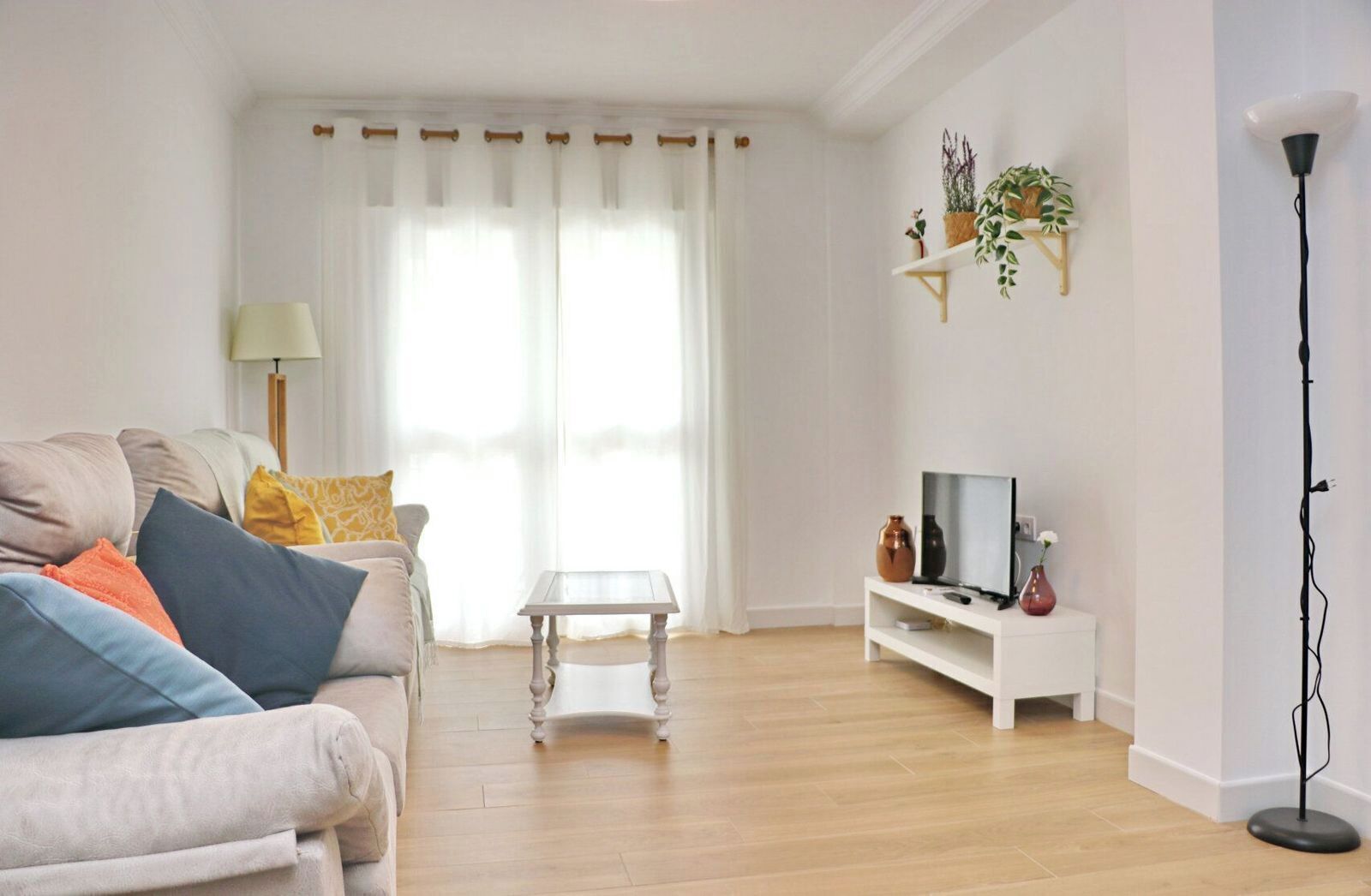 Een woonkamer met een bank, een salontafel, een televisie op een dressoir en een vloerlamp.