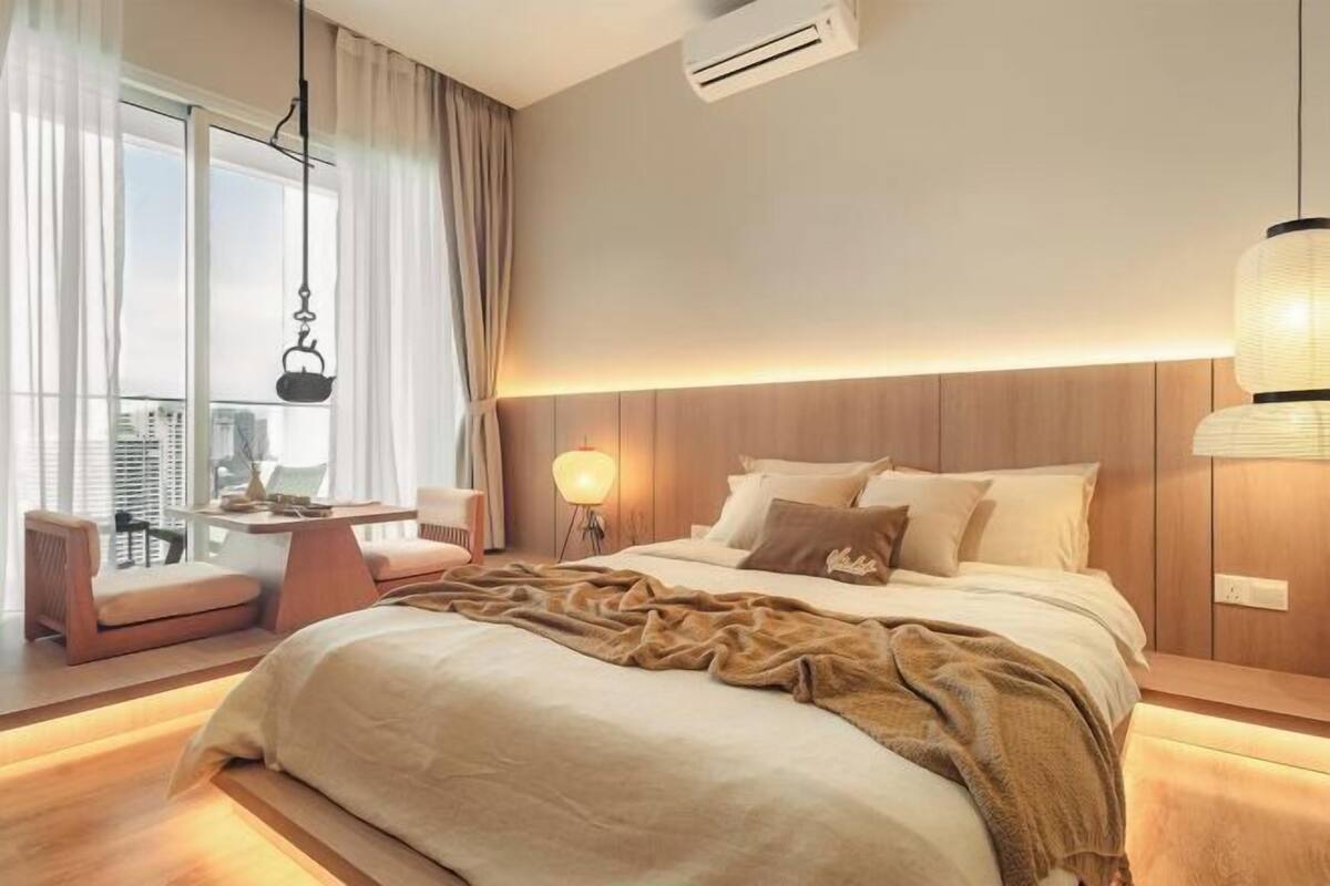 Une chambre d’hôtel moderne avec un grand lit, un bureau avec une chaise, un luminaire suspendu et une vue sur la ville.