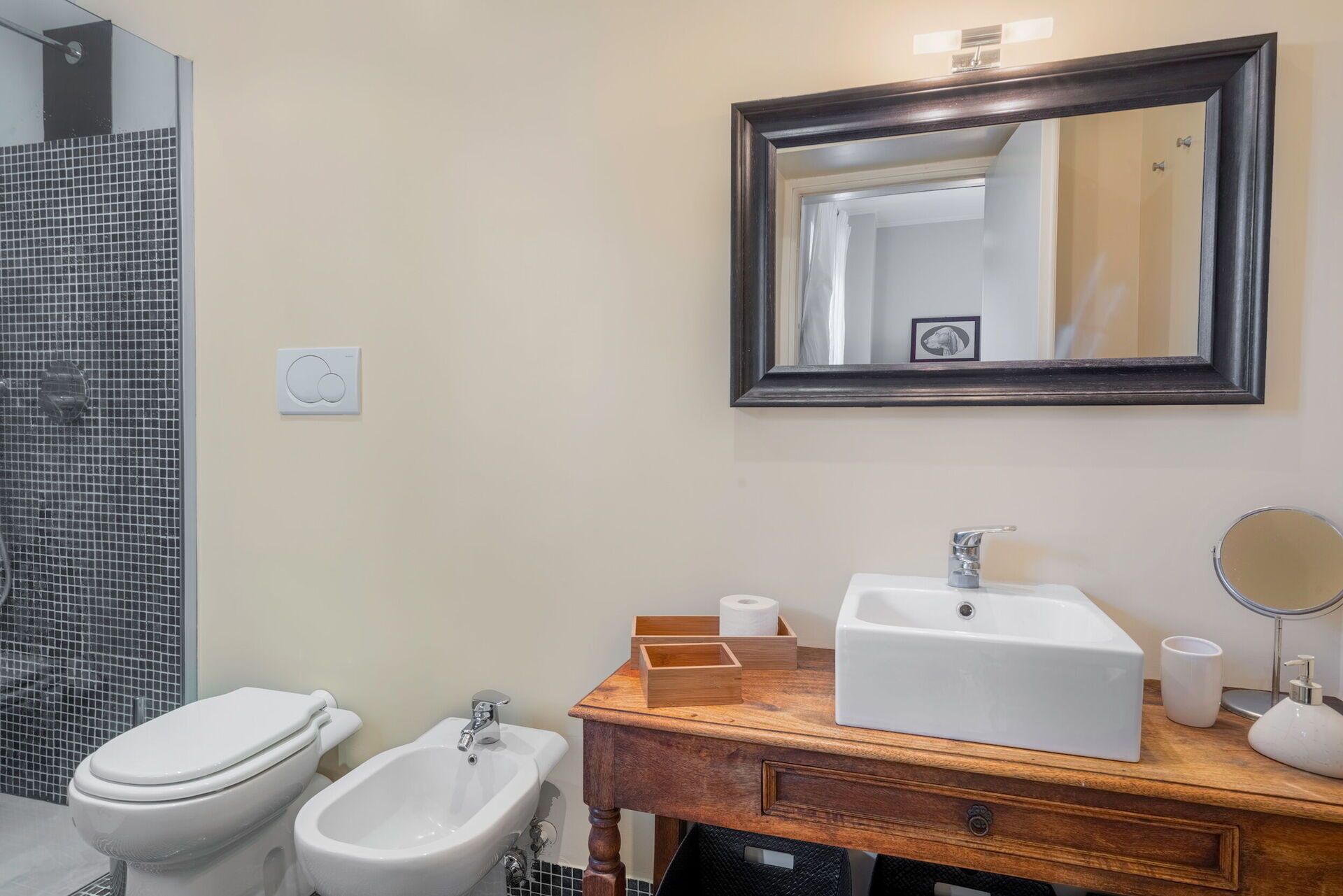 Un baño con inodoro, bidé, lavabo, espejo y un espejo enmarcados en la pared.