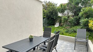 En uteplats med ett svart bord och stolar, en krukväxt och en trädgård i bakgrunden.